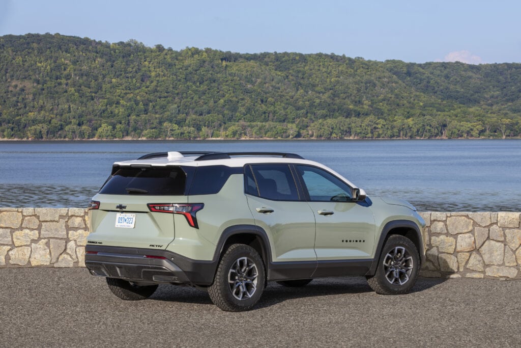Rear 3/4 view of a 2025 Chevrolet Equinox ACTIV in Cacti Green with Summit White roof parked near a large body of water.