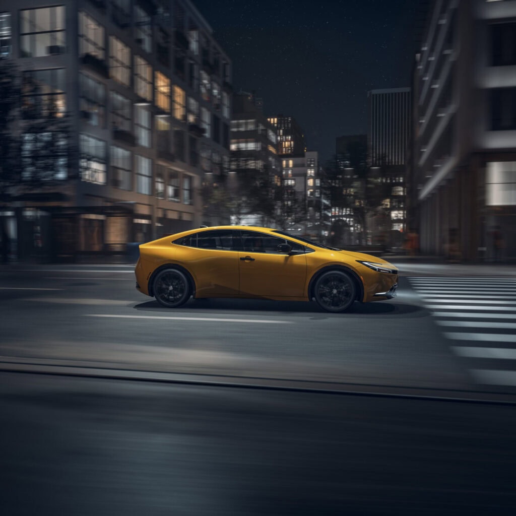 2026 Toyota Prius nightshade in yellow driving through the city at night