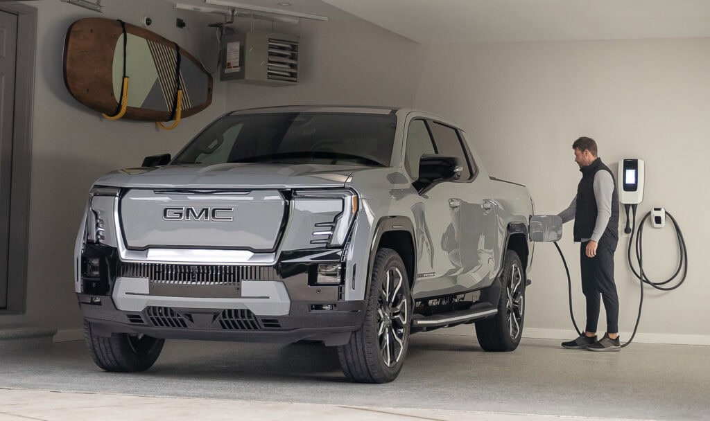 A man plugs in the 2024 GMC Sierra EV Denali Edition 1 to an electric vehicle charger inside a garage.