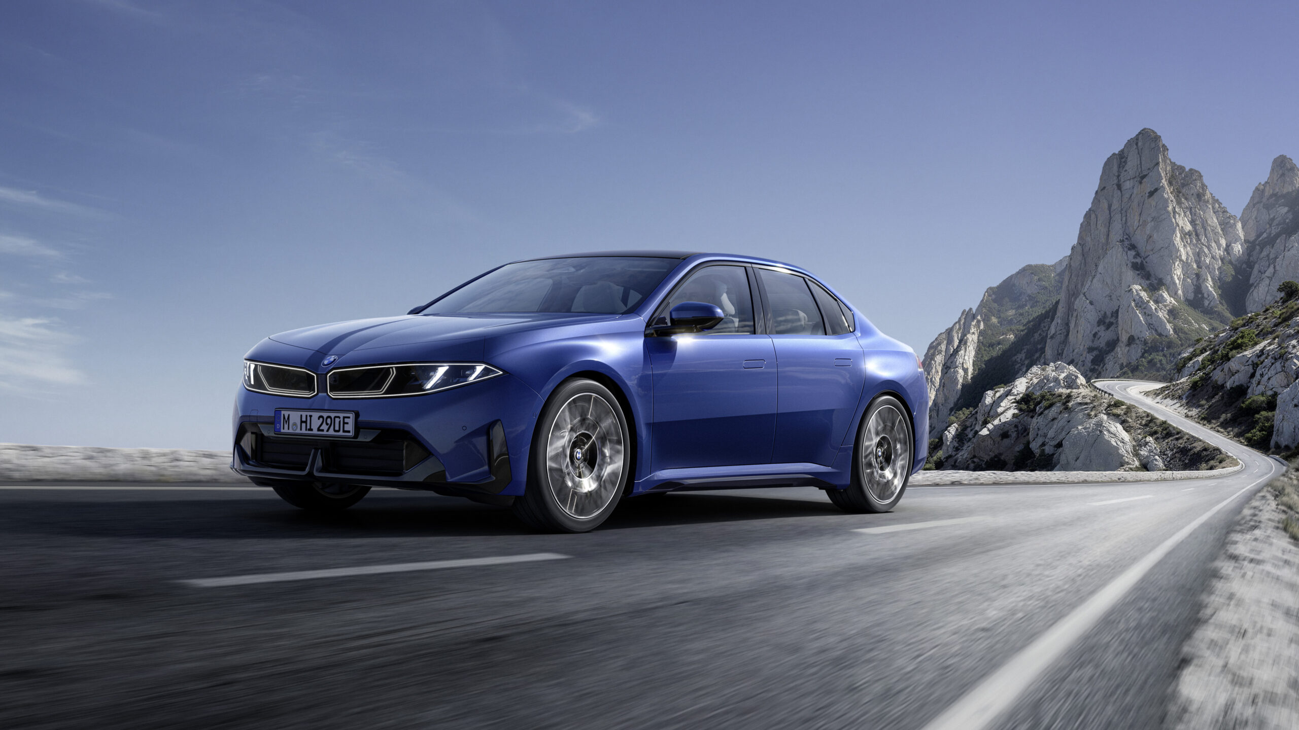 Blue BMW i3 50 xDrive on a winding road beside rocky coastal cliffs