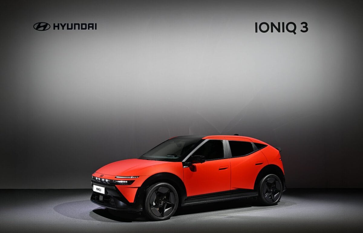 Orange Hyundai IONIQ 3 displayed against a gray wall with the model name overhead.