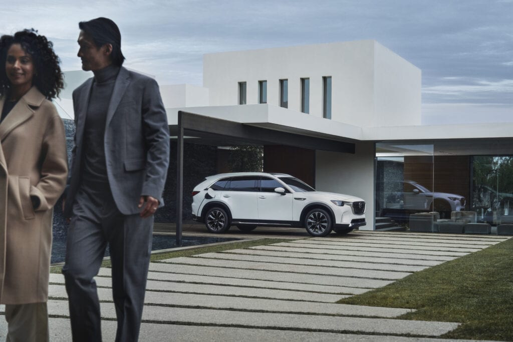 White Mazda CX-90 PHEV plugged in beside a modern house