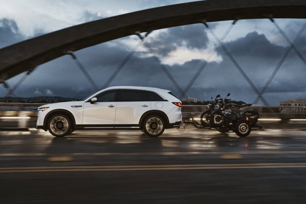 White Mazda CX-90 PHEV towing a motorcycle on a trailer