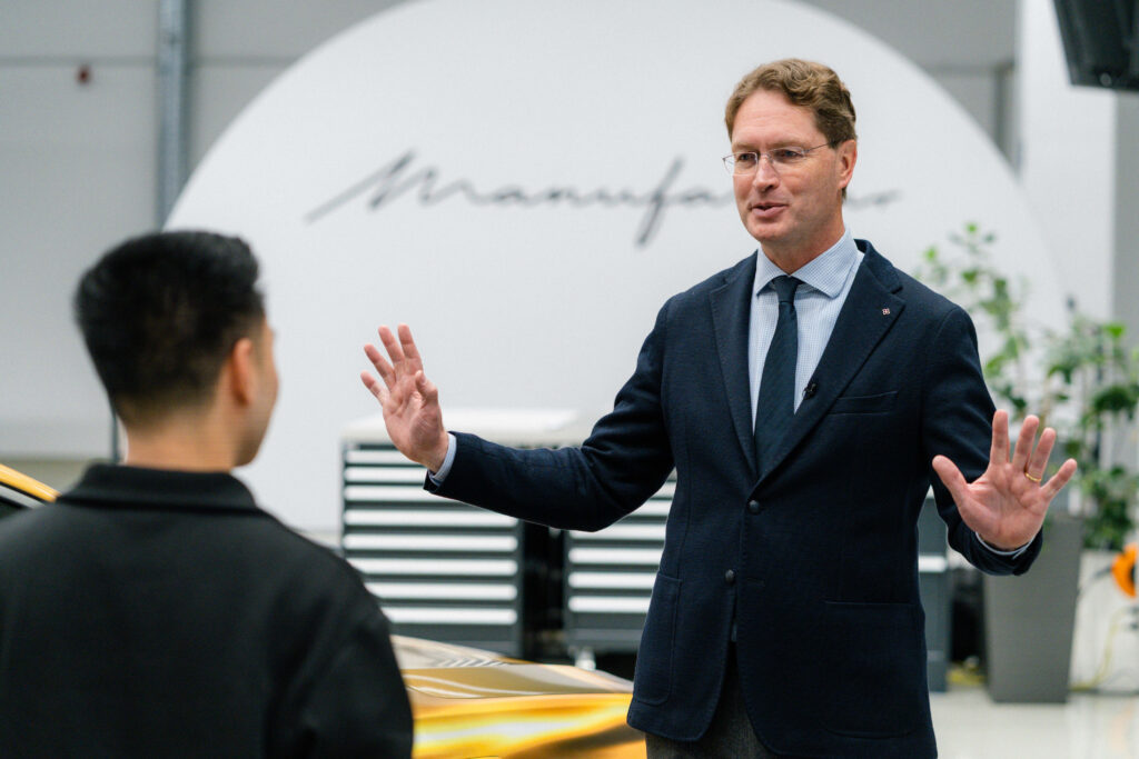 Ola Källenius speaking beside a camouflaged Mercedes-Benz S-Class.