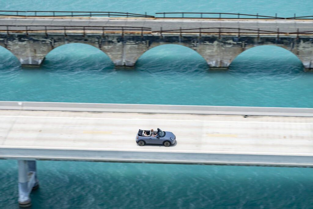 Mini convertible crossing a bridge with bright blue water beneath it