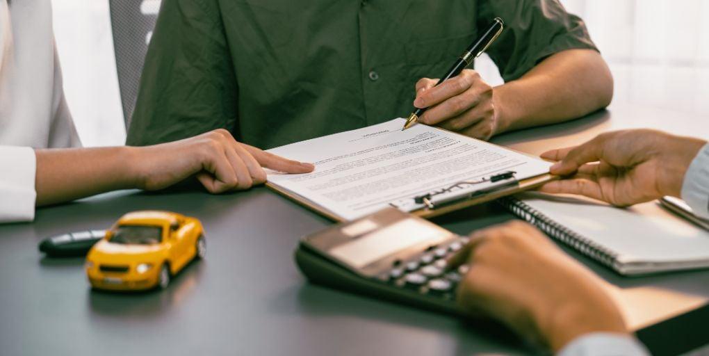A couple signing their auto loan on a clipboard in an office