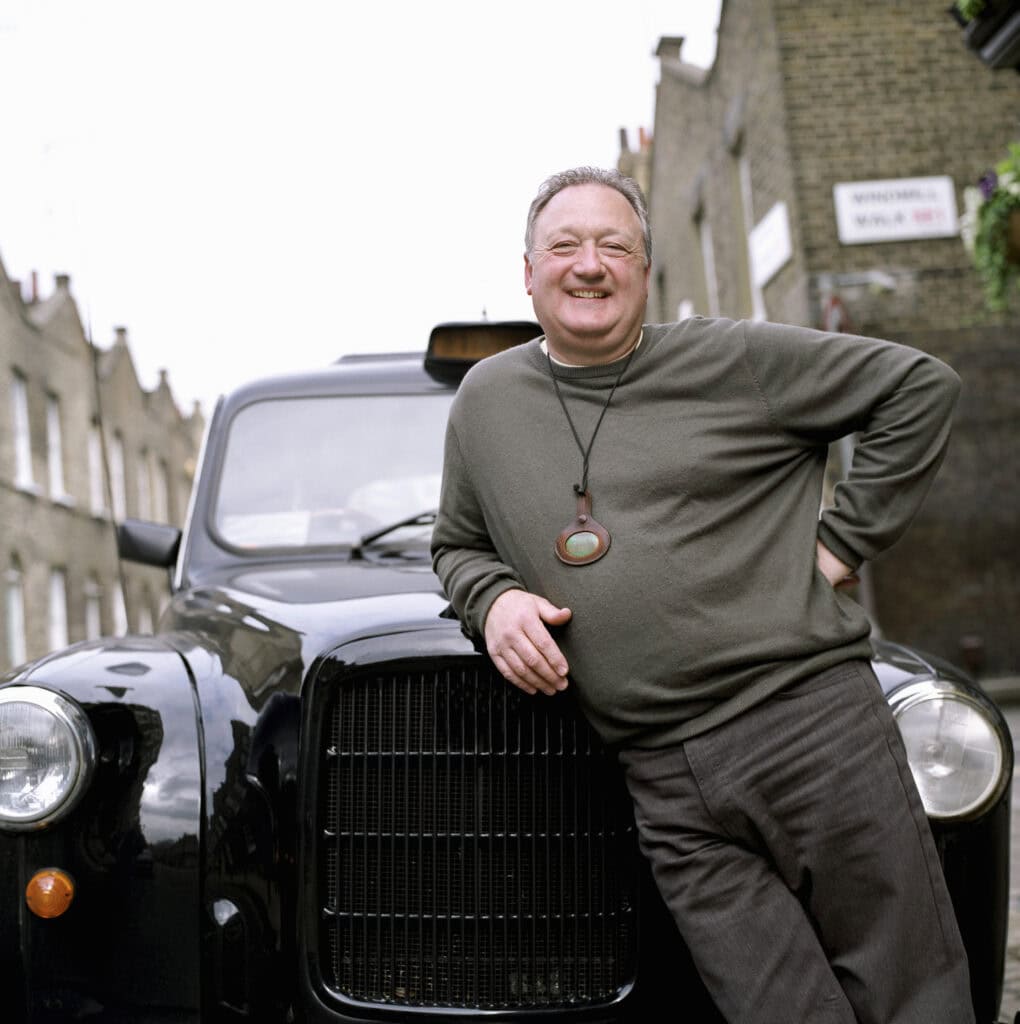 Portrait of taxi driver leaning against black cab, London, UK